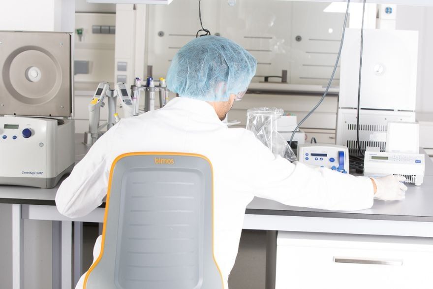 Labormitarbeiter an einem Labortisch auf einem ergonomischen Laborstuhl der Marke Bimos