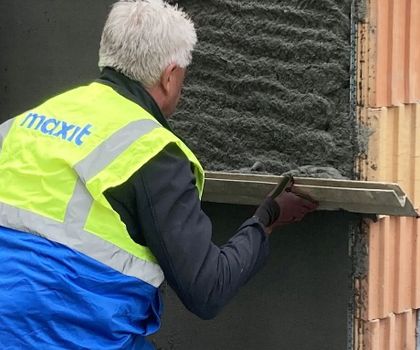 Maxit - Pflanzkohle an der Wand Ein Arbeiter mit einer neongeleben Schutzwesete streicht mit einem Maurerbrett Maxit IP 18 ML C an einer Wand glatt