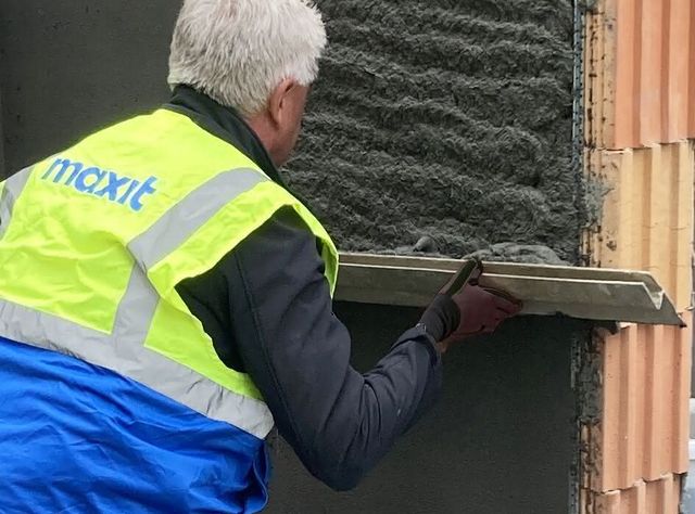Ein Arbeiter mit einer neongeleben Schutzwesete streicht mit einem Maurerbrett Maxit IP 18 ML C an einer Wand glatt
