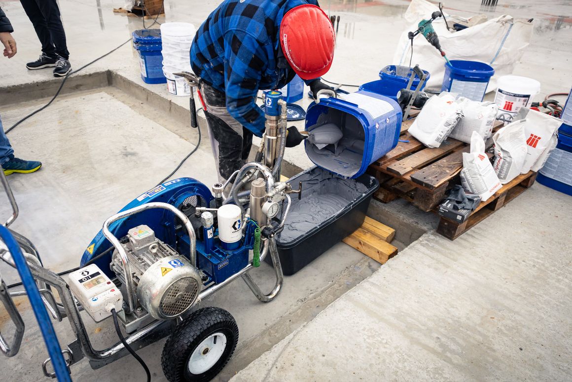 Die angemischte Bauwerksabdichtung Aquafin-RB400 wird händisch in den Vorratsbehälter der Airless-Spritzmaschine gefüllt.