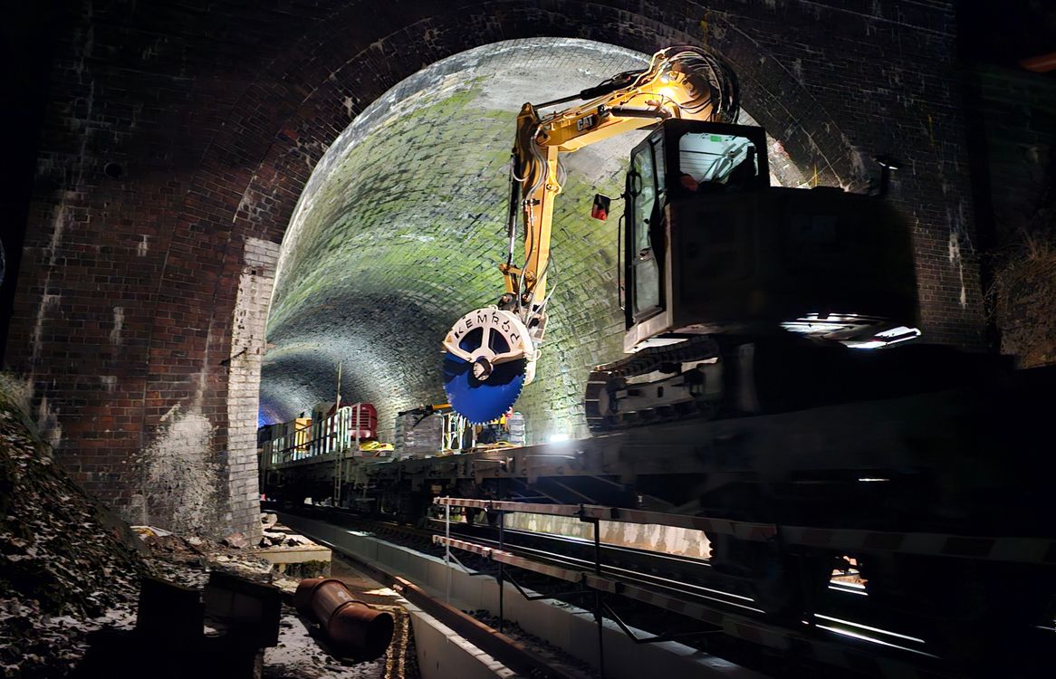Ein 8-t-Bagger mit einer KEMROC-Diamantsäge KDS 30 fährt auf einem Plattformwagen in den Elleringhauser Tunnel ein. Seine Aufgabe bestand darin, Beton-Kabelkanäle am Tunnelfuß zu zerschneiden.
