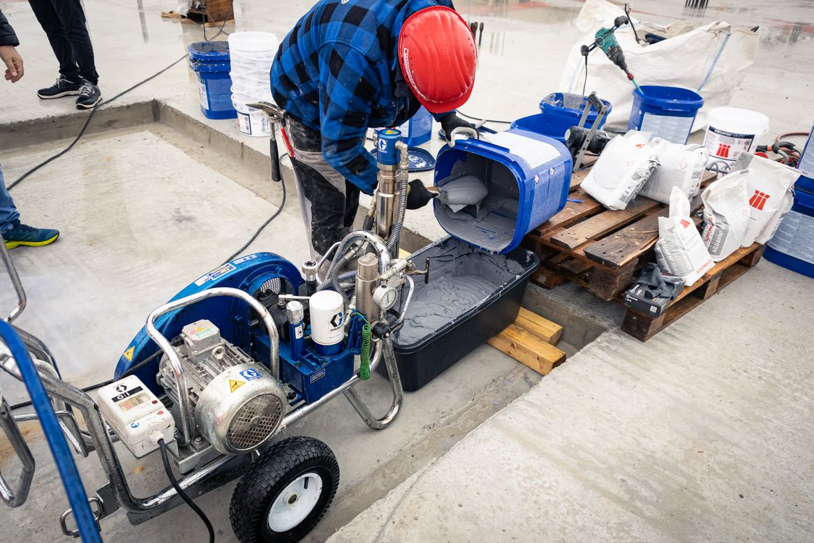 Die angemischte Bauwerksabdichtung Aquafin-RB400 wird händisch in den Vorratsbehälter der Airless-Spritzmaschine gefüllt.