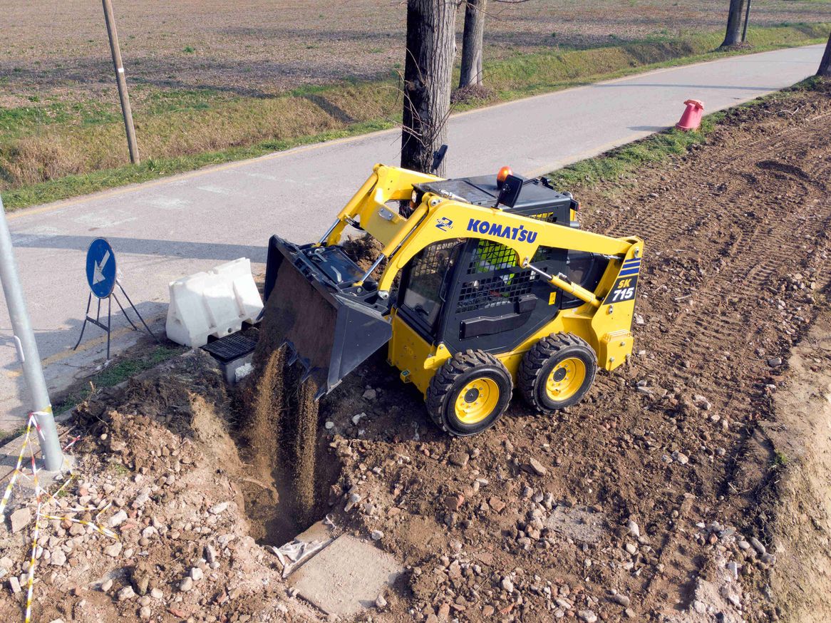 Durch die Ausstattungsmöglichkeit mit unterschiedlichsten Anbaugeräten, zeichnet sich der SK715-8 im Einsatz auf Baustellen, im Industriebereich oder in Häfen durch seine unvergleichliche Vielseitigkeit aus Ein Komtasu SK715-8 im Einsatz auf einer GaLaBau-Baustelle