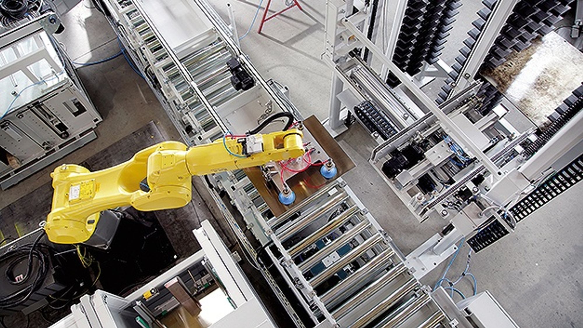 A robot uses a suction gripper to move separator plates between the handling lift of the vertical storage system and the roller conveyor.