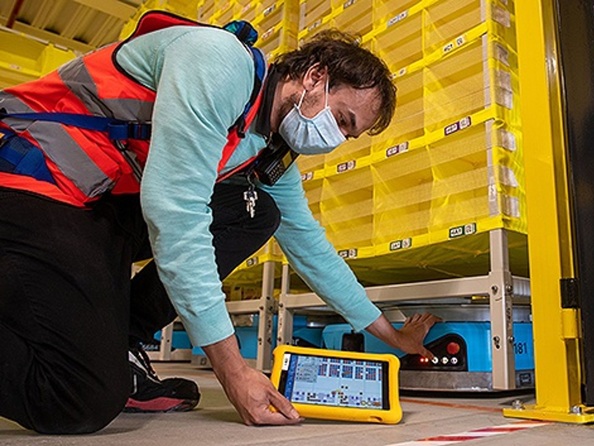 Philipp Weiß kontrolliert bei der Firma Amazon mit einem Tablet Logistikroboter.
