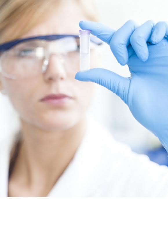Labormitarbeiterin schaut auf ein Probenröhrchen