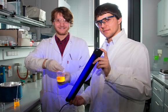Fabian Zechmeister (links) und Maximilian Raab demonstrieren die Fluoreszenz einer Perylenbisimidlösung. (Copyright: TU Wien)