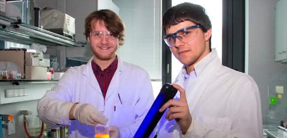 Fabian Zechmeister (links) und Maximilian Raab demonstrieren die Fluoreszenz einer Perylenbisimidlösung. (Copyright: TU Wien)
