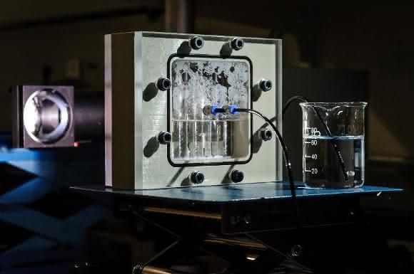 Testaufbau des Prototyps der photoelektrochemischen Wasserspaltung: Das komplette System befindet sich in einem mit Wasser (angereichert mit Kalilauge) gefüllten Behälter. Durch die Bestrahlung der Solarzellen mit einer Tageslichtlampe wird in ihnen eine Spannung von 1,8 Volt generiert. Mit der erzeugten Spannung wird das Elektrolysesystem (auf der Vorderseite, mit Anoden und Kathoden aus Nickelschaum) betrieben, das das Wasser in Wasserstoff und Sauerstoff spaltet. Copyright: Tobias Dyck/Forschungszentrum Jülich