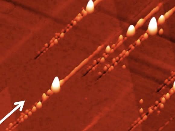 Nanostrukturen nach dem Ionenbeschuss: Der Pfeil zeigt die Richtung der Ionen an: Zunächst ensteht ein Graben mit Nanohillocks an beiden Seiten, ein besonders großer Hügel zeigt den Impakt-Punkt an, danach ist noch eine Erhebung entlang des Pfades zu sehen, den das Ion unter der Oberfläche zurücklegt. (Copyright: TU Wien)