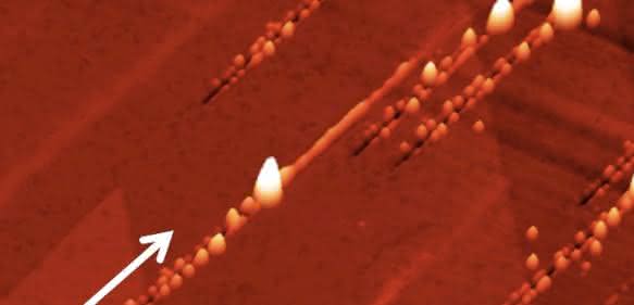 Nanostrukturen nach dem Ionenbeschuss: Der Pfeil zeigt die Richtung der Ionen an: Zunächst ensteht ein Graben mit Nanohillocks an beiden Seiten, ein besonders großer Hügel zeigt den Impakt-Punkt an, danach ist noch eine Erhebung entlang des Pfades zu sehen, den das Ion unter der Oberfläche zurücklegt. (Copyright: TU Wien)
