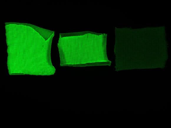 Machbarkeitsstudie – Textilien auf Cellulosebasis wurden mit einem grün-fluoreszierenden Markerprotein + Cellulose-Anker ausgerüstet. Baumwolle (links), Viskose (mitte), Negativkontrolle = grün-fluoreszierendes Protein ohne Cellulose-Anker (rechts). (© Foto Hohenstein Institute)