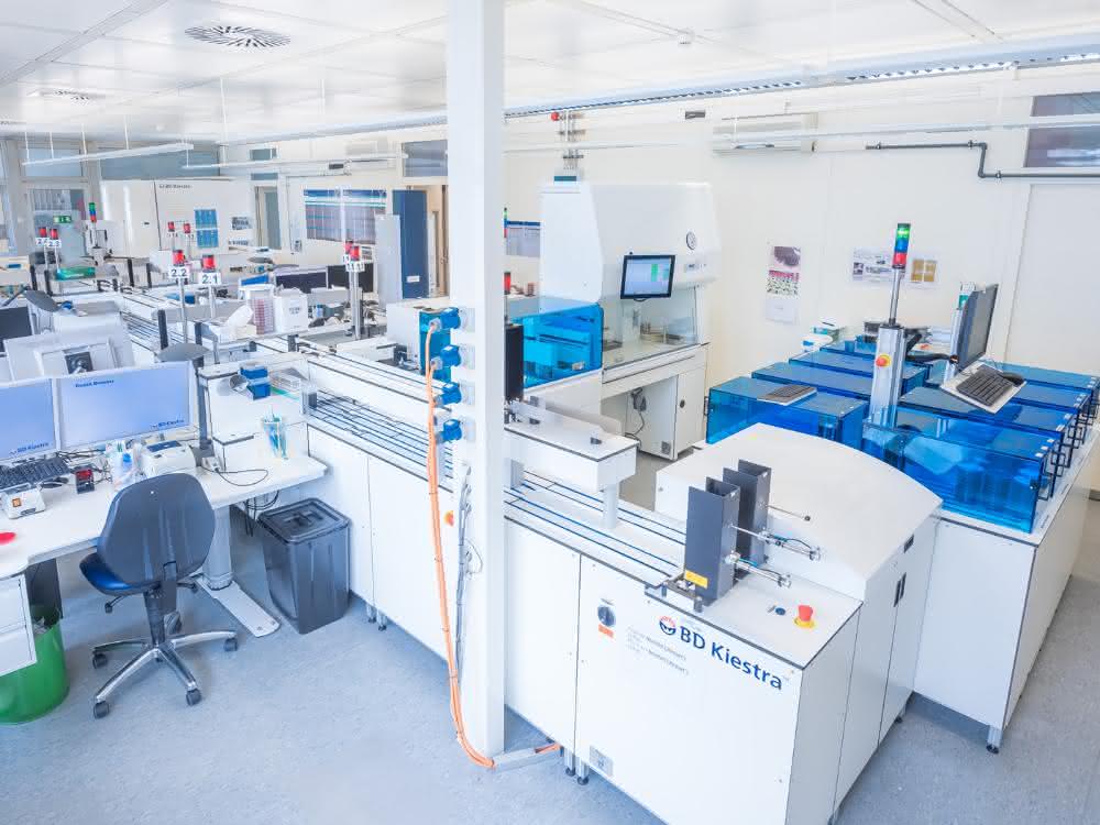 Bild 1: Anlage TLA: SorterA und BarcodA (rechts), InoculA mit Sterilbank (Mitte), ProceedA (Vordergrund) und Verarbeitungsplätze (Workstations) (links), ReadA Compacts (Hintergrund links). Bild 1: Anlage im mikrobiologischen Labor