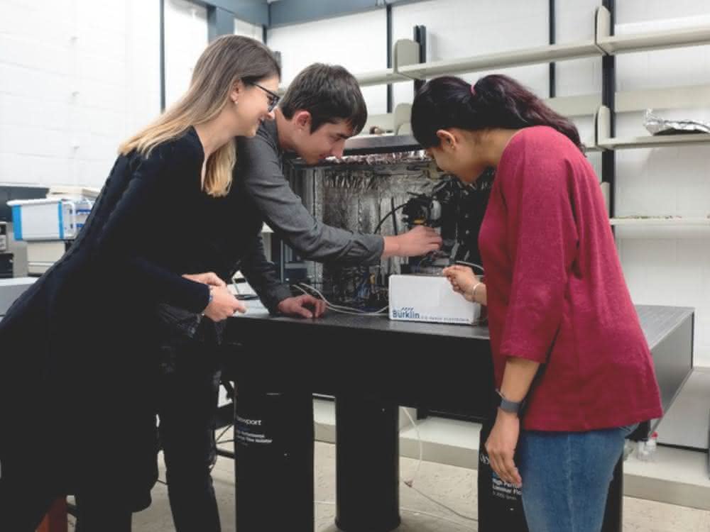 Corina Andronescu, Tsvetan Tarnev und Harshitha Barike Ayappa besprechen ein Experiment am elektrochemischen Rasterzellmikroskop.