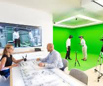 Virtuelle Realität im „Autodesk VR Lab“ München: 2 Personen stehend mit VR-Brillen, auf einem Bildschirm an der Wand ein virtuelles Bild, und 2 Personen sitzen am Schreibtisch.