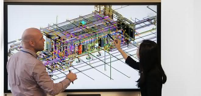 Virtuelle Zusammenarbeit mit der nativen BIM-Lösung Revit: TÜV SÜD Korea und TÜV SÜD Advimo arbeiten gleichzeitig an einem Labor-Projekt, wobei sich die Spezialisten auf unterschiedlichen Kontinenten befinden. Vor einem Bildschirm mit digitalem Modell stehen eine Frau und ein Mann, die sich besprechen.