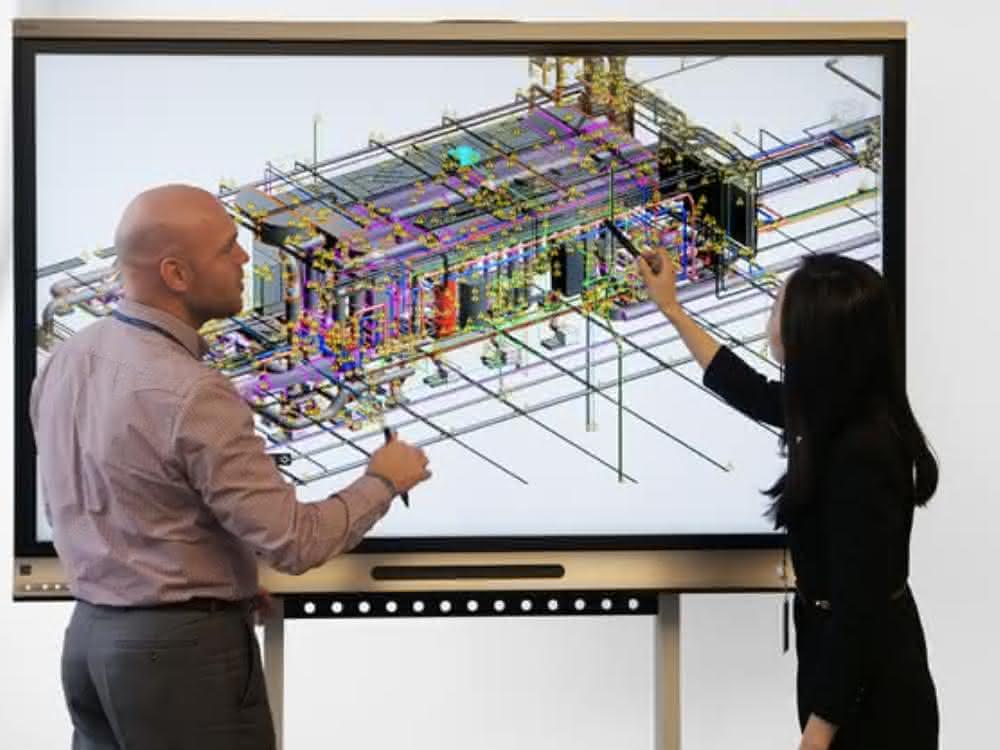 Virtuelle Zusammenarbeit mit der nativen BIM-Lösung Revit: TÜV SÜD Korea und TÜV SÜD Advimo arbeiten gleichzeitig an einem Labor-Projekt, wobei sich die Spezialisten auf unterschiedlichen Kontinenten befinden. Vor einem Bildschirm mit digitalem Modell stehen eine Frau und ein Mann, die sich besprechen.