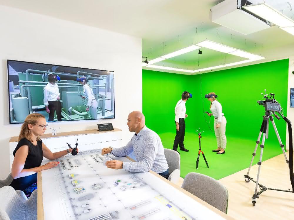 Virtuelle Realität im „Autodesk VR Lab“ München: 2 Personen stehend mit VR-Brillen, auf einem Bildschirm an der Wand ein virtuelles Bild, und 2 Personen sitzen am Schreibtisch.