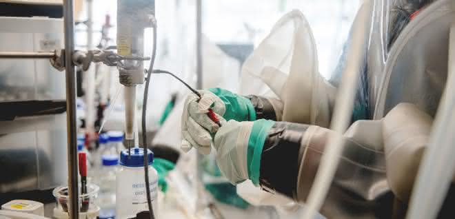 Hydrogenasen sind sehr empfindlich gegenüber Sauerstoff, daher müssen die Experimente mit ihnen in einer abgeschotteten Umgebung stattfinden. Blick in eine Workstation, in der ein Labormitarbeiter mit Handschuhen durch zwei Eingriffbereiche hindurch hantiert.