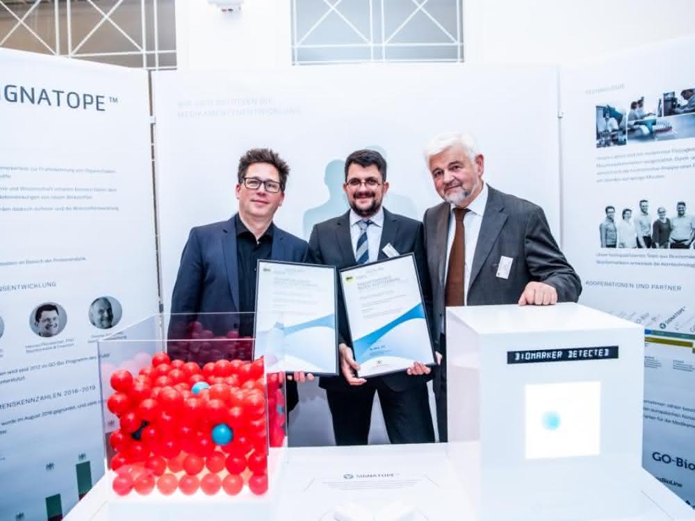 Oliver Pötz (links) und Hannes Planatscher (Mitte, beide Signatope) nahmen die Auszeichnung vom Stuttgarter Regierungspräsidenten Wolfgang Reimer entgegen. Signatope-Mitarbeiter am Messestand.