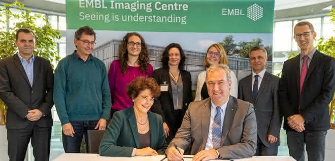 Gruppenfoto von Vertretern von Leica Microsystems und vom EMBL; im Vordergrund am Tisch sitzend Edith Hard und Markus Lusser bei der Unterzeichnung der Vereinbarung