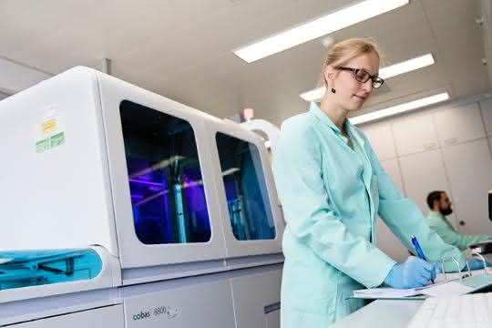 Labormitarbeiterin bei der Arbeit, dahinter ein Cobas-System