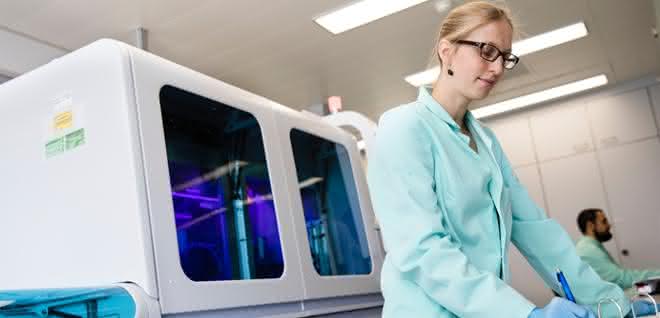 Labormitarbeiterin bei der Arbeit, dahinter ein Cobas-System