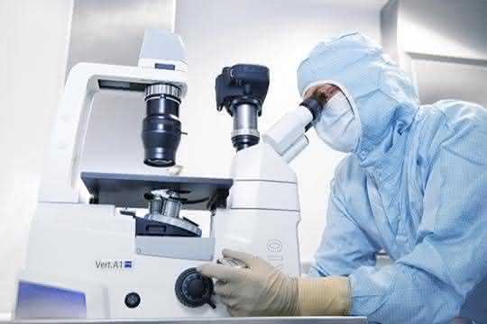 Forscher mit Schutzkleidung schaut in ein Mikroskop