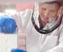 Biobanken sammeln, lagern und verarbeiten qualitätsgesichert und datenschutzkonform humane Bioproben wie Blut oder Gewebe, die sie der Forschung bereitstellen. Labormitarbeiterin mit Gesichtsschutz und blauen Handschuhen hält Probenbehältnis
