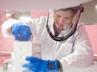 Biobanken sammeln, lagern und verarbeiten qualitätsgesichert und datenschutzkonform humane Bioproben wie Blut oder Gewebe, die sie der Forschung bereitstellen. Labormitarbeiterin mit Gesichtsschutz und blauen Handschuhen hält Probenbehältnis