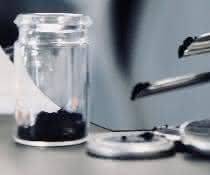 Mit neuen Materialien möchten die Forschenden sichere und langlebige Hochleistungszellen möglich machen. Schwarzes Pulver im Präparateglas und Knopfzellen