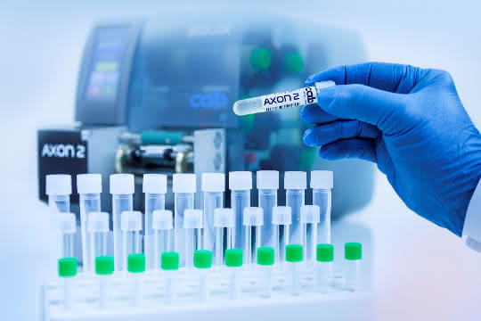 Probenröhrchen mit bedrucktem Etikett, im Hintergrund der Etikettierer AXON 2