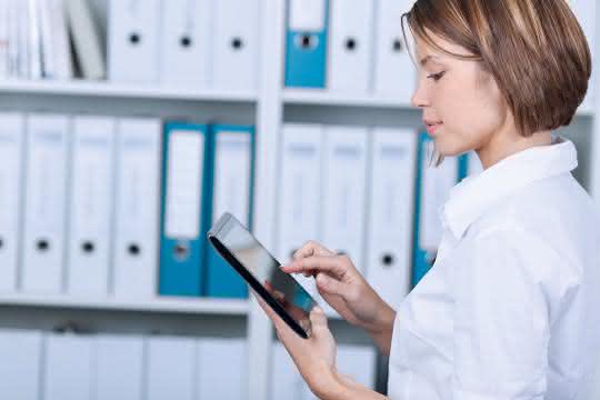 Frau am Tablet vor Regal mit Aktenordnern