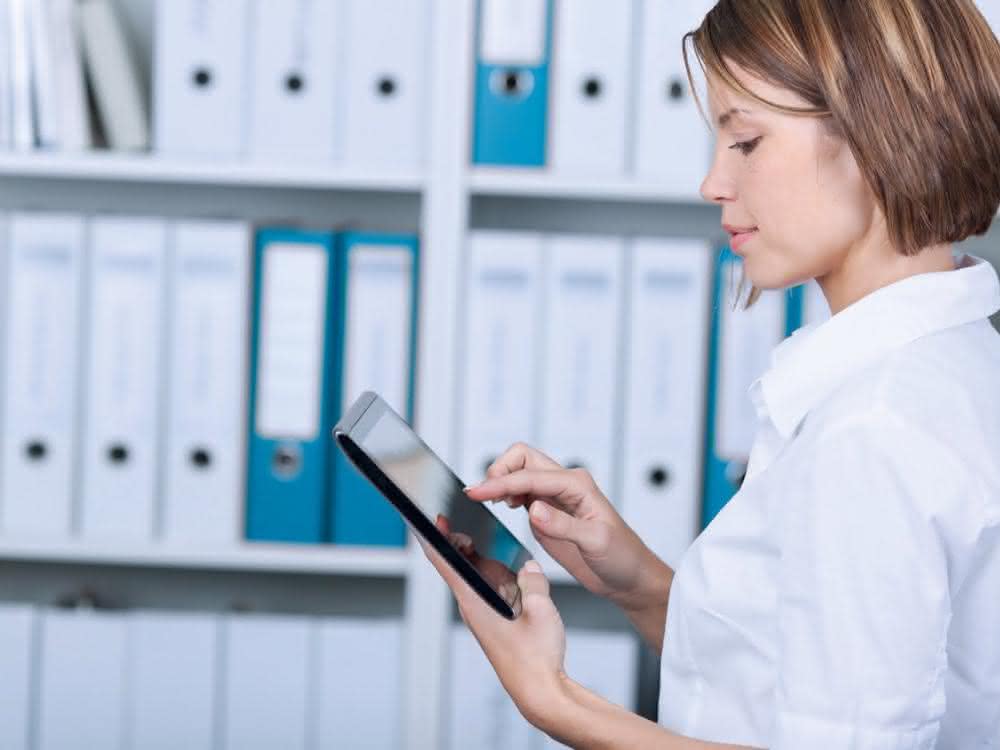 Frau am Tablet vor Regal mit Aktenordnern