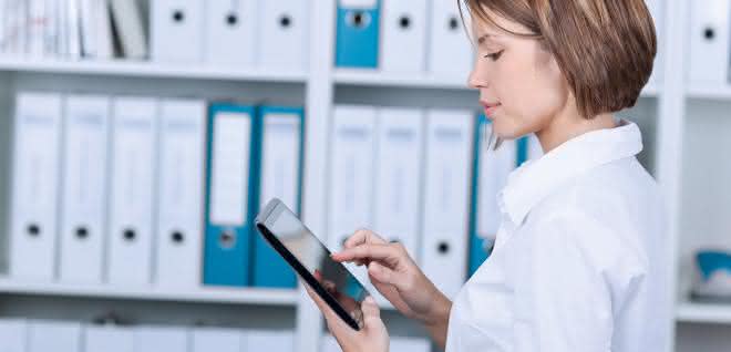 Frau am Tablet vor Regal mit Aktenordnern